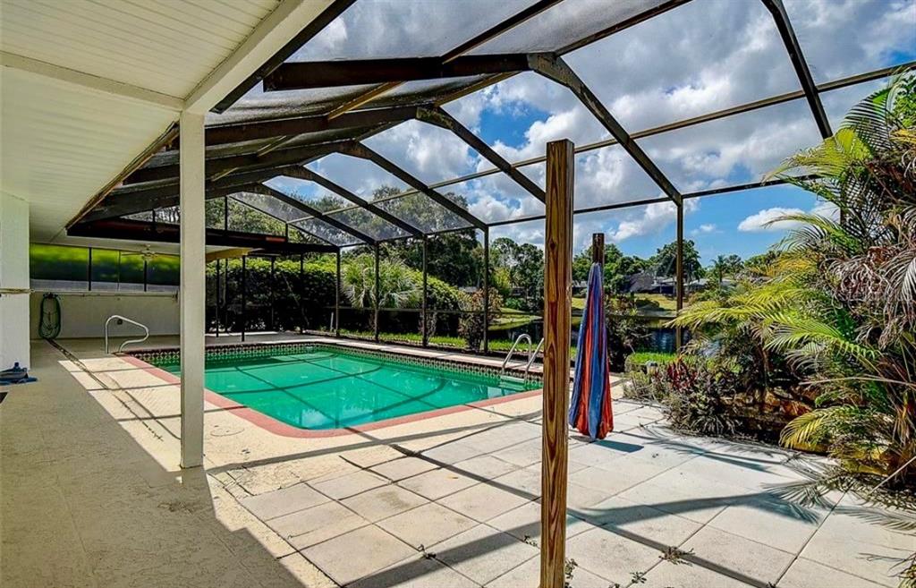 A screened-in patio features a swimming pool, a ceiling fan, and a view of water — 2876 LAKE VALENCIA BOULEVARD E, PALM HARBOR, FL