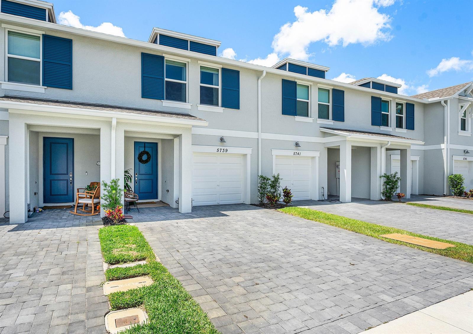 A row of multi-story townhouses features gray stucco siding, blue shutters, and paved driveways — 5739 SE Edgewater Circle, Stuart FL 34997, STUART, FL