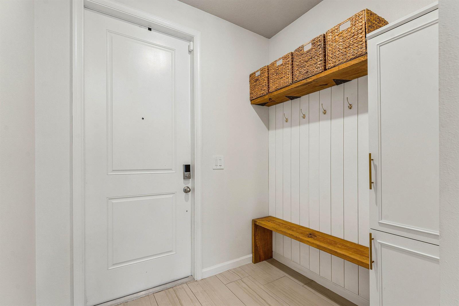 An entryway features a white door, a wooden bench, wall hooks, and overhead woven baskets — 5739 SE Edgewater Circle, Stuart FL 34997, STUART, FL