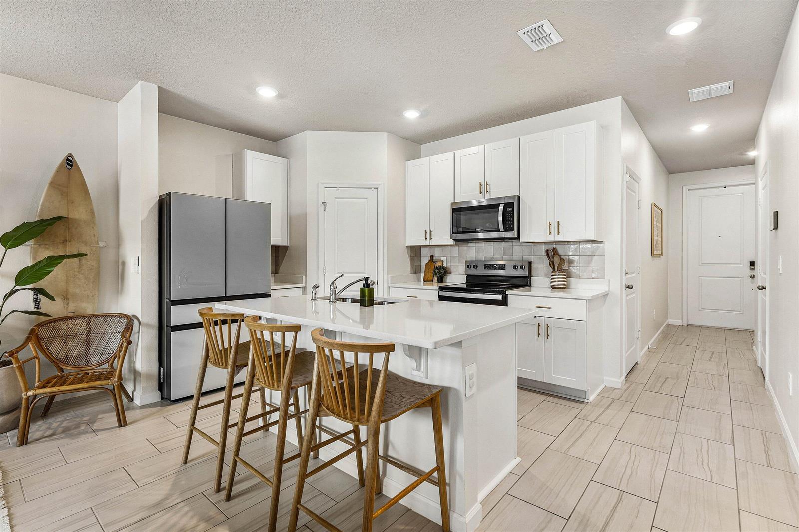 A modern kitchen features white cabinets, a quartz island with bar stools, and tile flooring — 5739 SE Edgewater Circle, Stuart FL 34997, STUART, FL