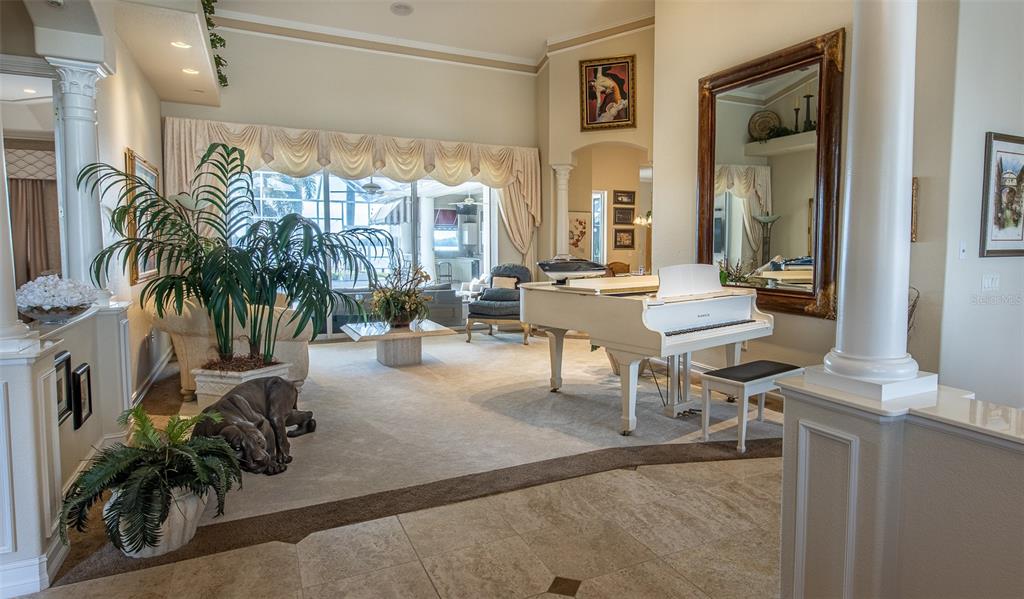 A living room features a white grand piano, a large mirror, and a sliding glass door — 17479 OHARA DRIVE, PORT CHARLOTTE, FL
