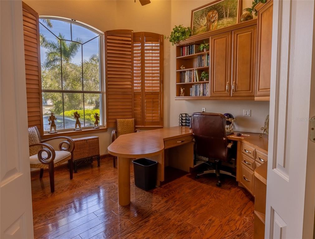 A home office with a wooden desk, built-in shelving, and a large arched window — 17479 OHARA DRIVE, PORT CHARLOTTE, FL