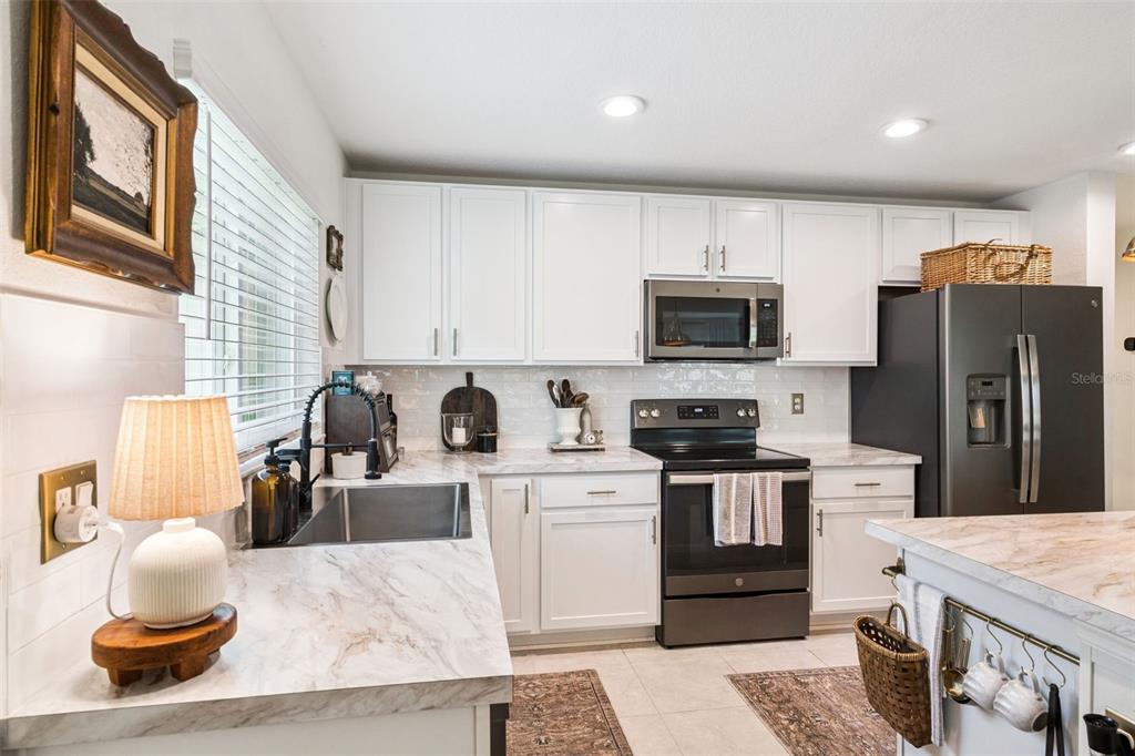 A kitchen features white cabinets, marble-look countertops, a black refrigerator, and a stainless steel sink — 1657 WILSON PRAIRIE CIRCLE, GROVELAND, FL