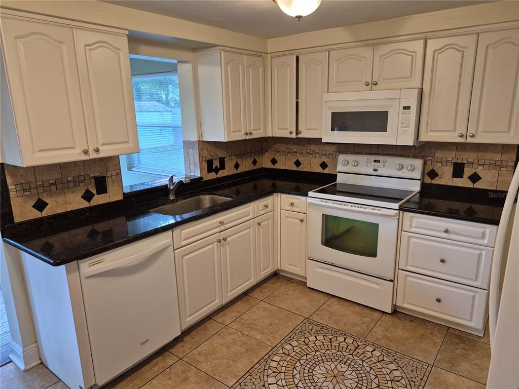 A kitchen with white cabinets, black granite countertops, a tiled backsplash, and white appliances — 6616 HONE STREET, NEW PORT RICHEY, FL