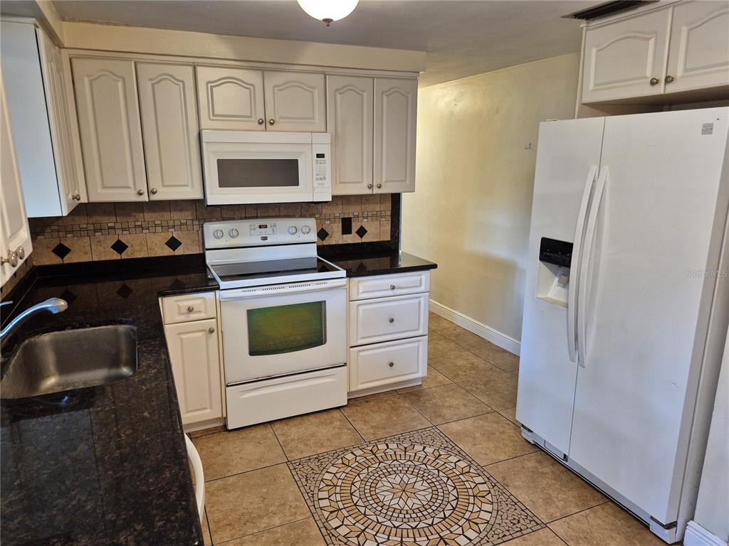 A kitchen features white cabinets, dark granite countertops, a white appliance suite, and tiled flooring — 6616 HONE STREET, NEW PORT RICHEY, FL