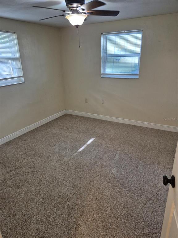 An empty bedroom with beige walls, gray carpet, two windows with blinds, and a ceiling fan — 6616 HONE STREET, NEW PORT RICHEY, FL