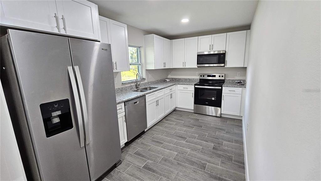 A kitchen features white cabinets, stainless steel appliances, granite countertops, and gray wood-look flooring — 604 LIME AVENUE, DUNDEE, FL