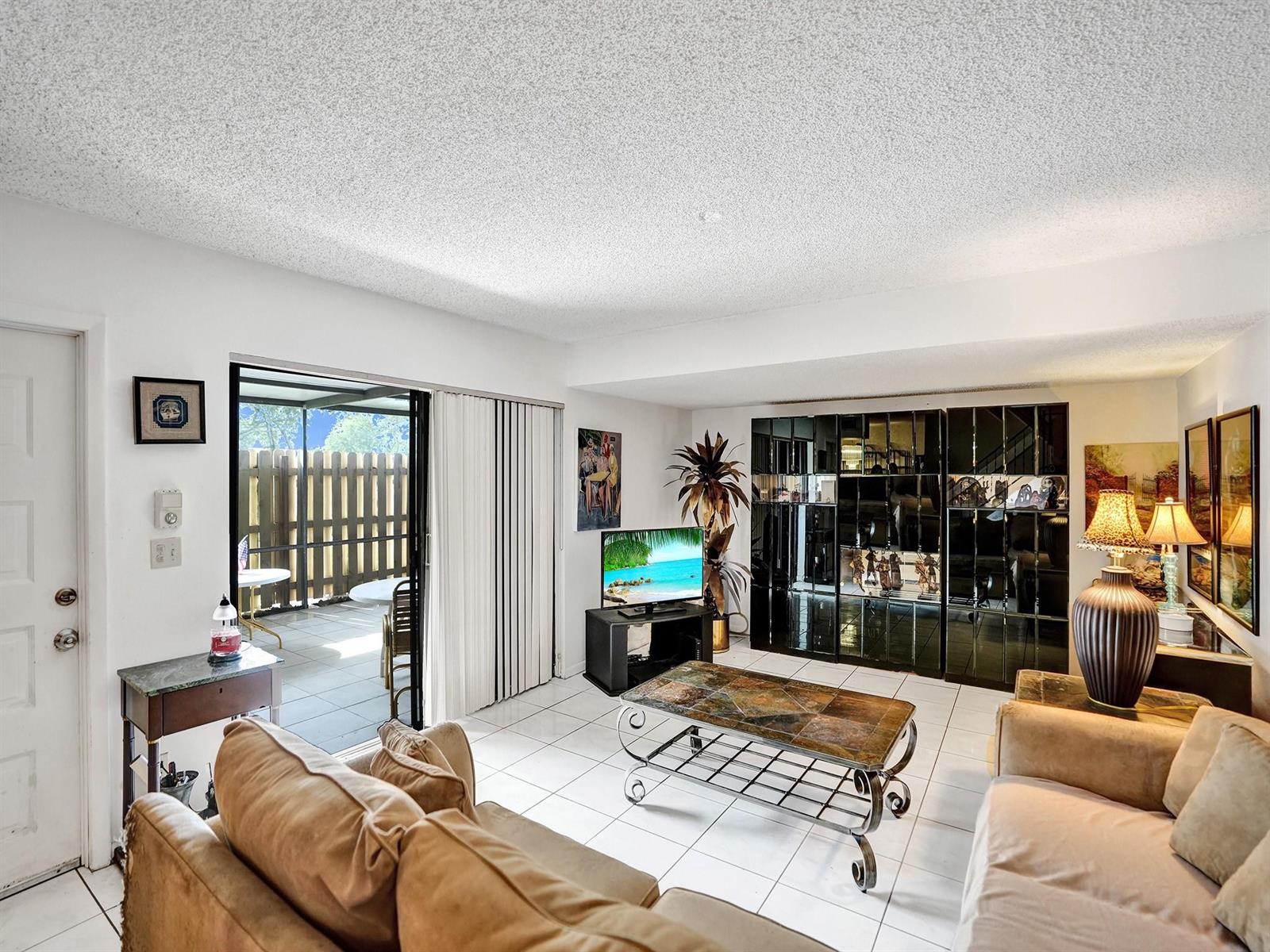 A living room with white tile floors, a sliding glass door, and a mirrored wall unit — 865 NW 29th Avenue # A, Delray Beach FL 33445, DELRAY BEACH, FL