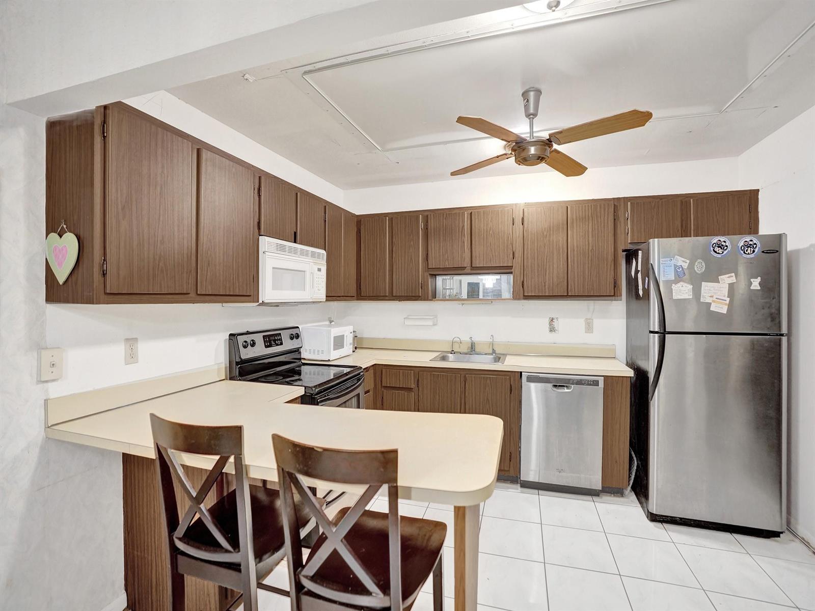 A kitchen features brown wood cabinets, a breakfast bar, stainless steel appliances, and white tile — 865 NW 29th Avenue # A, Delray Beach FL 33445, DELRAY BEACH, FL