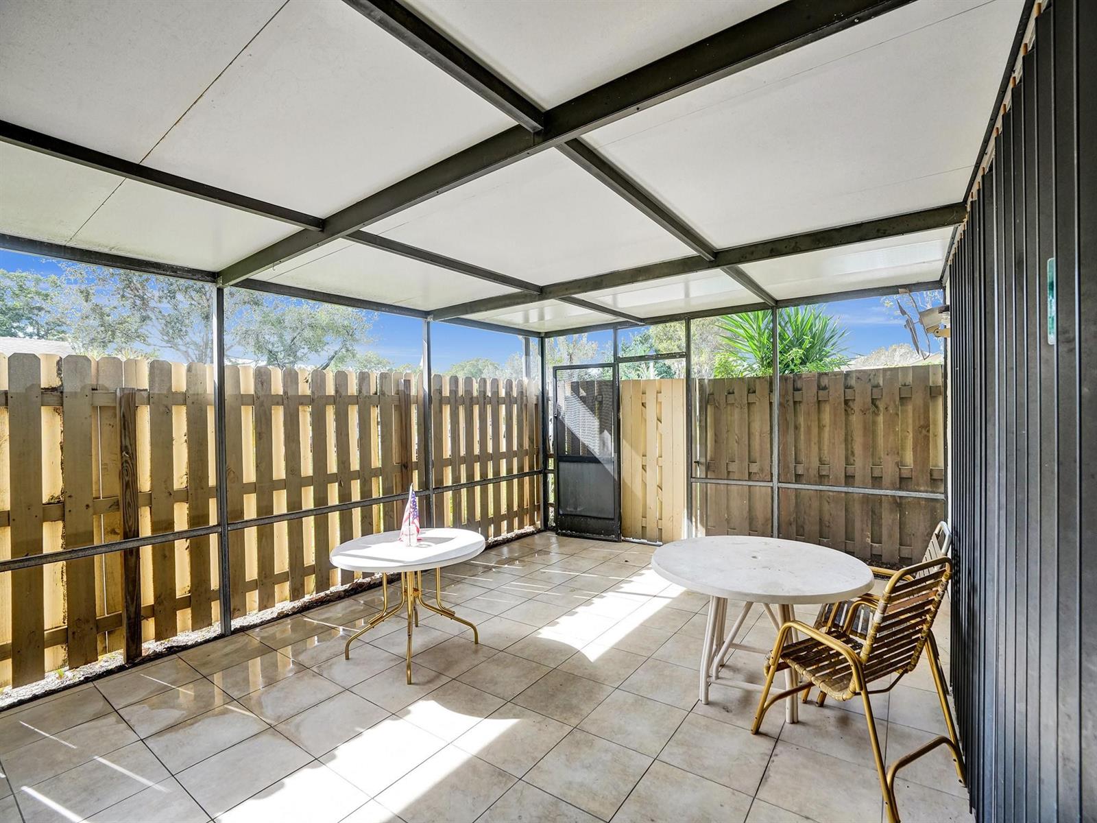 A screened-in patio features tiled flooring, a metal frame roof, and a wooden privacy fence — 865 NW 29th Avenue # A, Delray Beach FL 33445, DELRAY BEACH, FL
