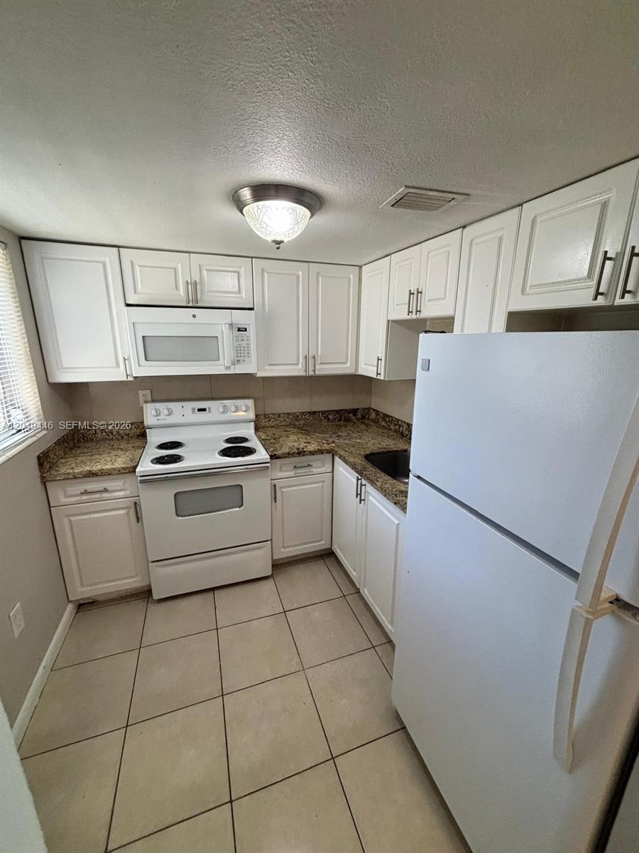A small kitchen features white cabinets, granite countertops, and white appliances — 3050 S Dixie Hwy # 402, Miami FL 33133, MIAMI, FL