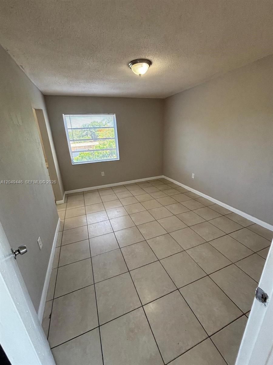 An empty room features light-colored tile flooring, gray walls, and a single window — 3050 S Dixie Hwy # 402, Miami FL 33133, MIAMI, FL