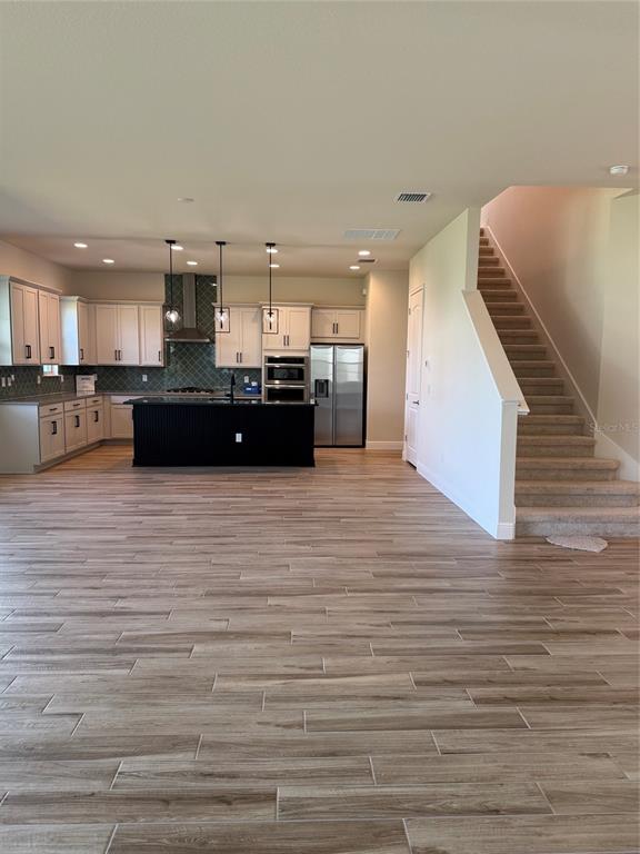 A kitchen with white cabinets, a black island, and wood-look tile flooring near a staircase — 5242 BUTTONSAGE DRIVE, ST CLOUD, FL