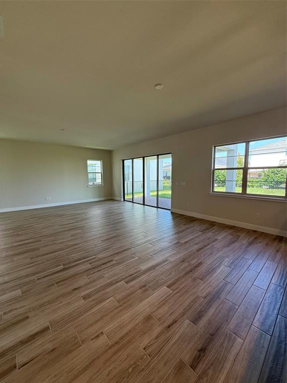 An empty living area features wood-look tile flooring, large windows, and sliding glass patio doors — 5242 BUTTONSAGE DRIVE, ST CLOUD, FL