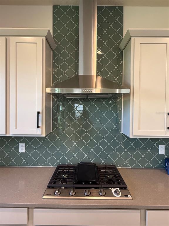 A kitchen features a stainless steel range hood, green arabesque tile backsplash, and white cabinets — 5242 BUTTONSAGE DRIVE, ST CLOUD, FL