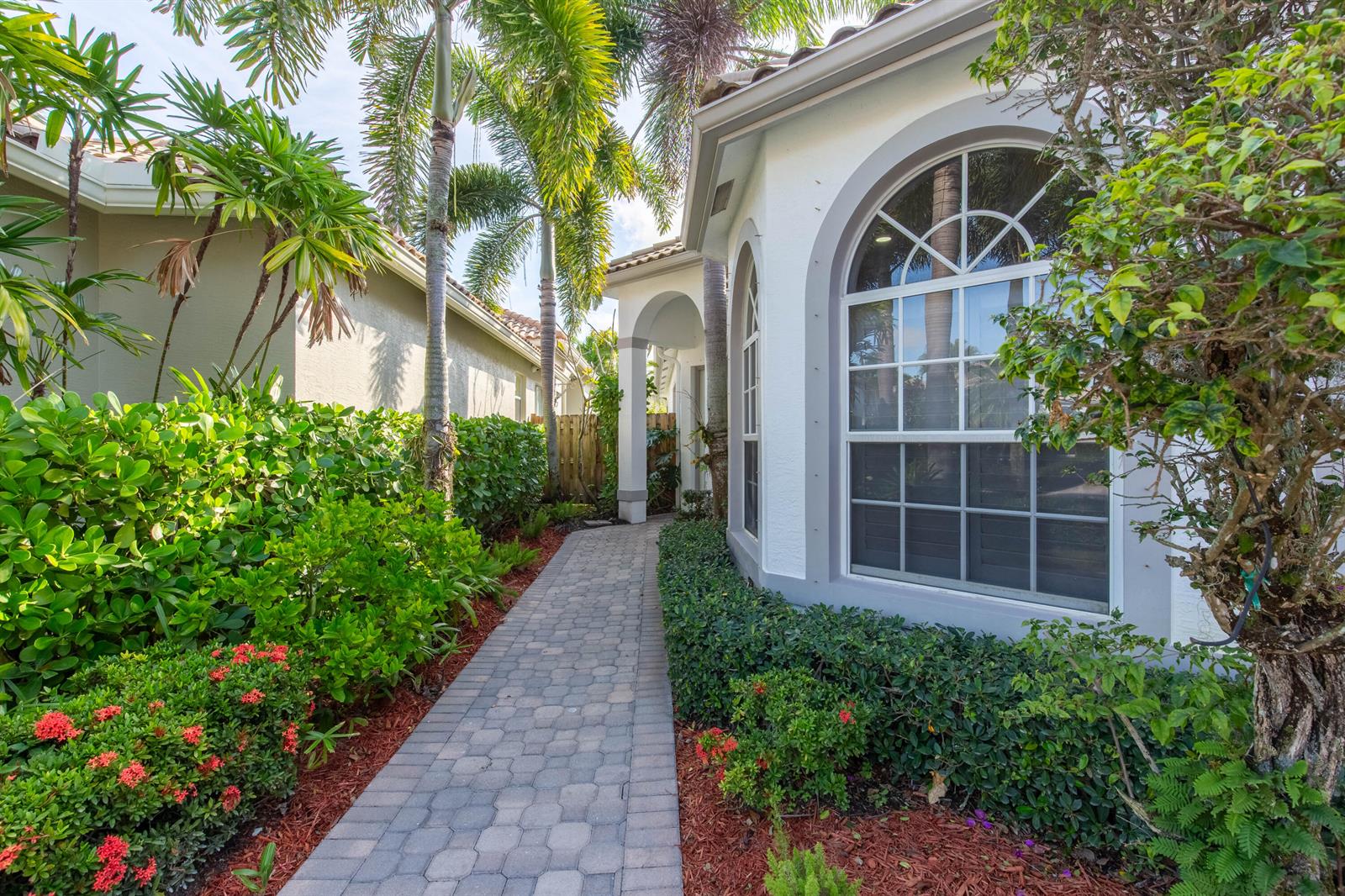 A stone walkway leads to the arched window and entrance of a white stucco house — 2443 Players Ct, Wellington FL 33414, WELLINGTON, FL
