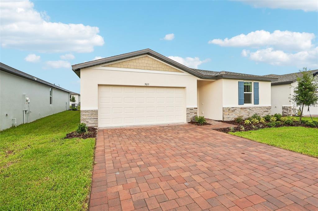 A single-story house features a two-car garage, stone accents, and a brick paver driveway — 5013 KAIA AVENUE, WINTER HAVEN, FL