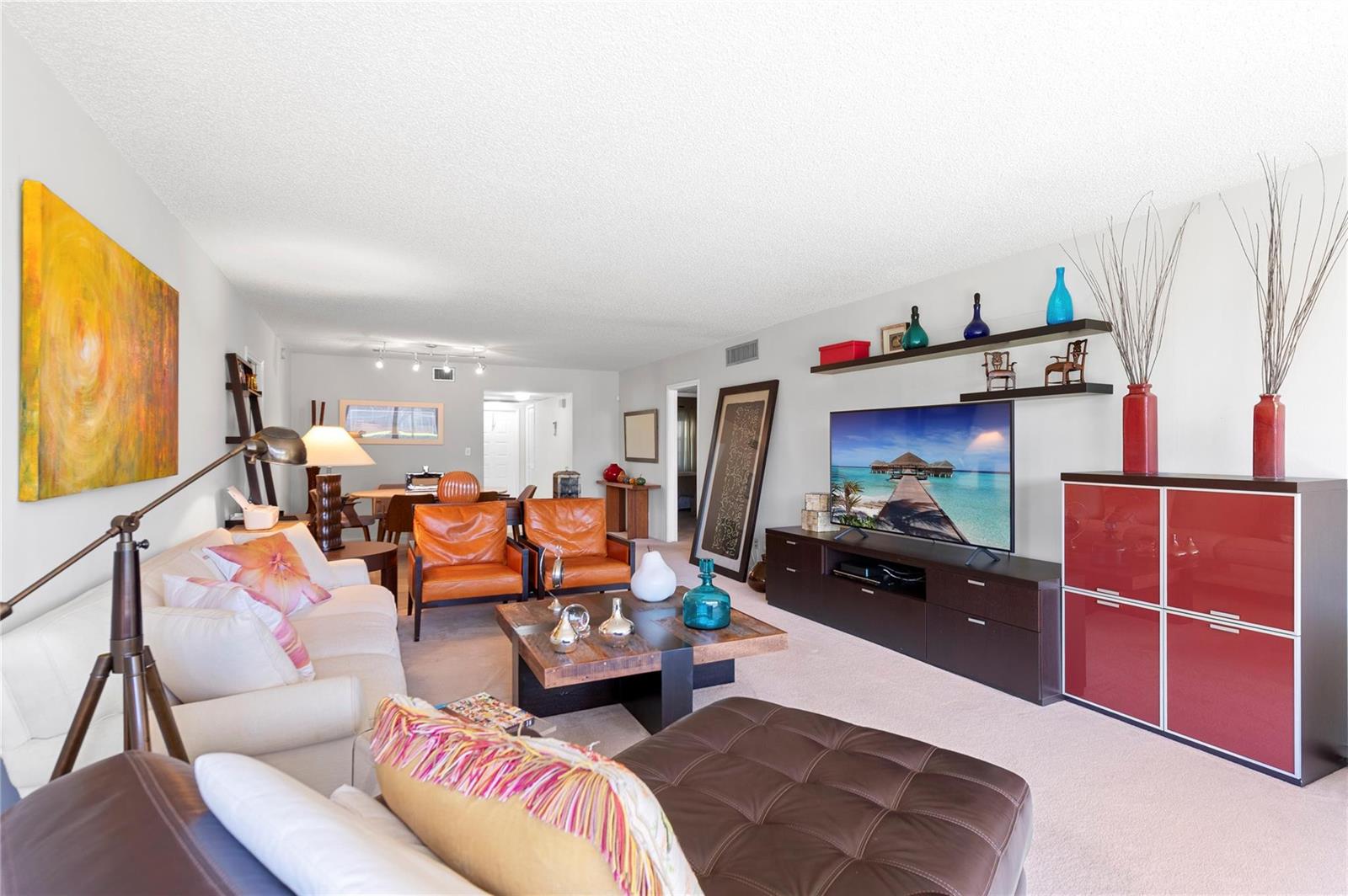 A living room features a white sofa, leather armchairs, a television, and red storage cabinets — 4240 Oaks Terrace # 105, Pompano Beach FL 33069, POMPANO BEACH, FL