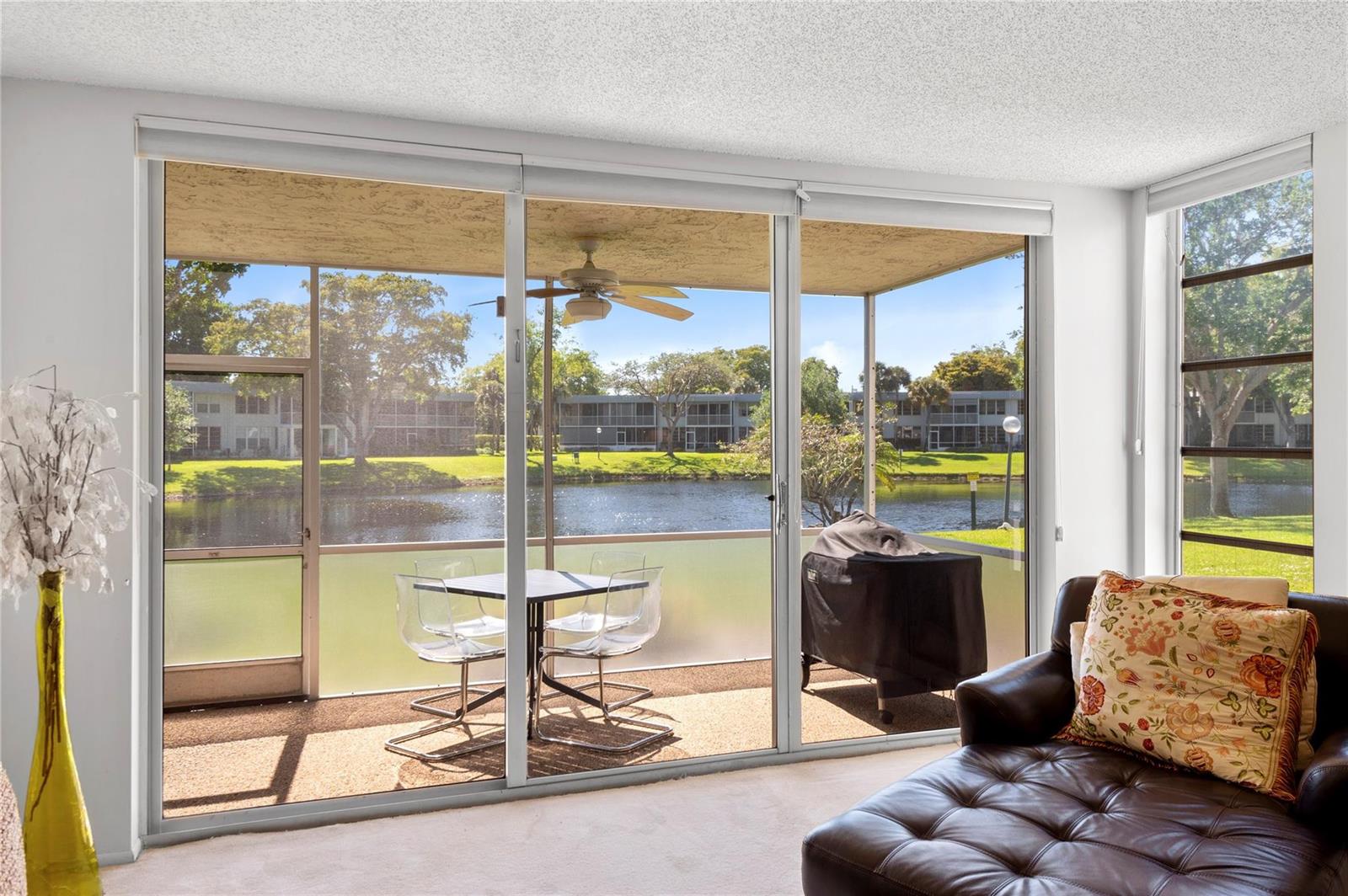 A living room features a sliding glass door opening onto a screened patio overlooking water — 4240 Oaks Terrace # 105, Pompano Beach FL 33069, POMPANO BEACH, FL