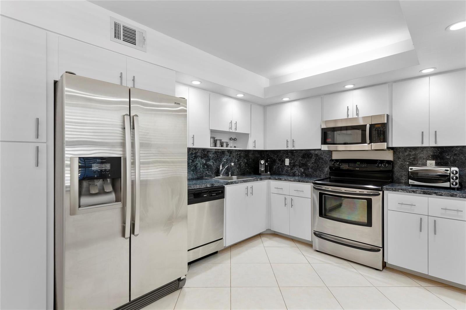 A kitchen with white cabinets, stainless steel appliances, and dark countertops on a tile floor — 4240 Oaks Terrace # 105, Pompano Beach FL 33069, POMPANO BEACH, FL