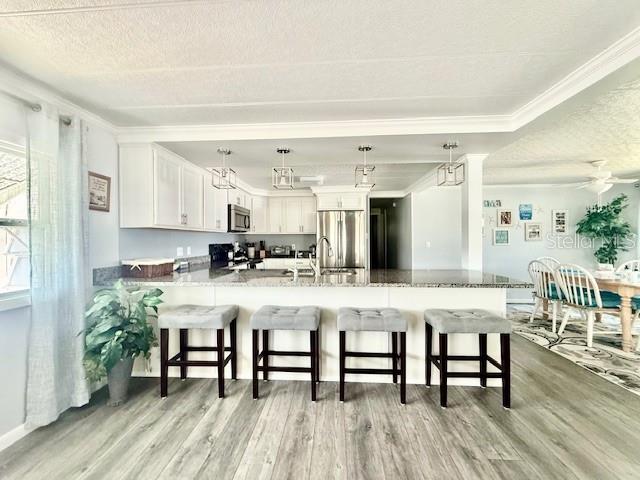 A kitchen features white cabinets, a breakfast bar with four stools, and wood-look flooring — 264 PHILADELPHIA BOULEVARD UNIT 51, PALM HARBOR, FL