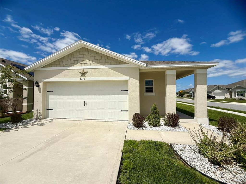 A single-story house with a two-car garage, beige stucco exterior, and a covered entryway — 2415 BRASSIE COURT, WINTER HAVEN, FL