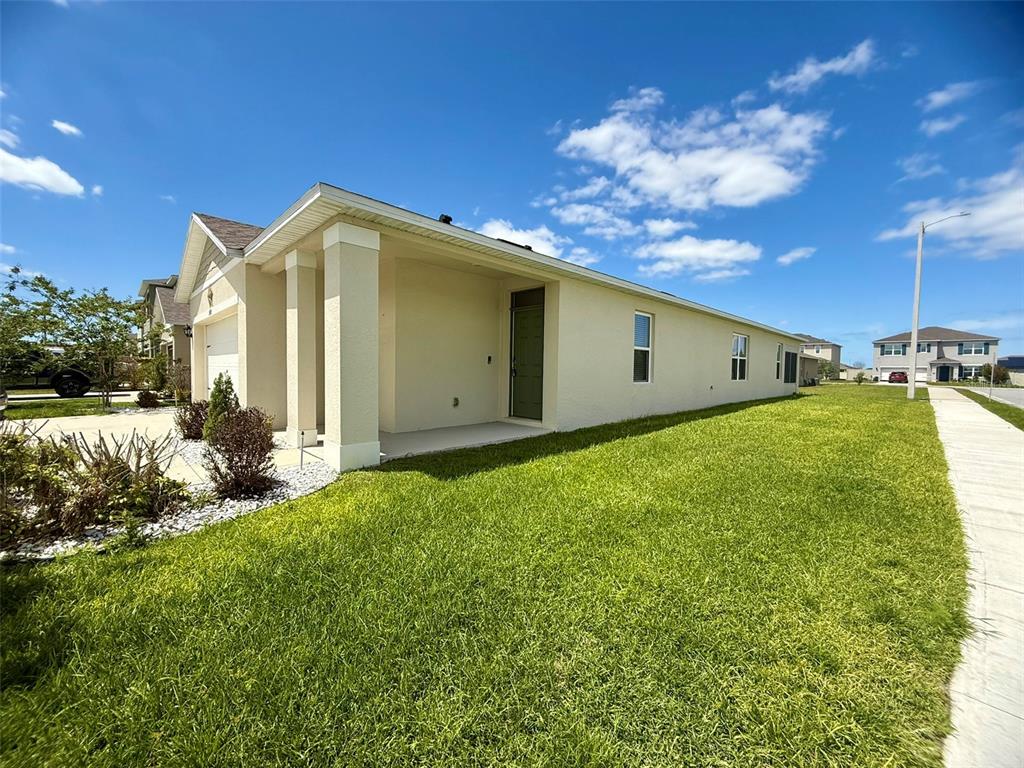 A side view of a beige single-story house with a covered entryway and green door — 2415 BRASSIE COURT, WINTER HAVEN, FL