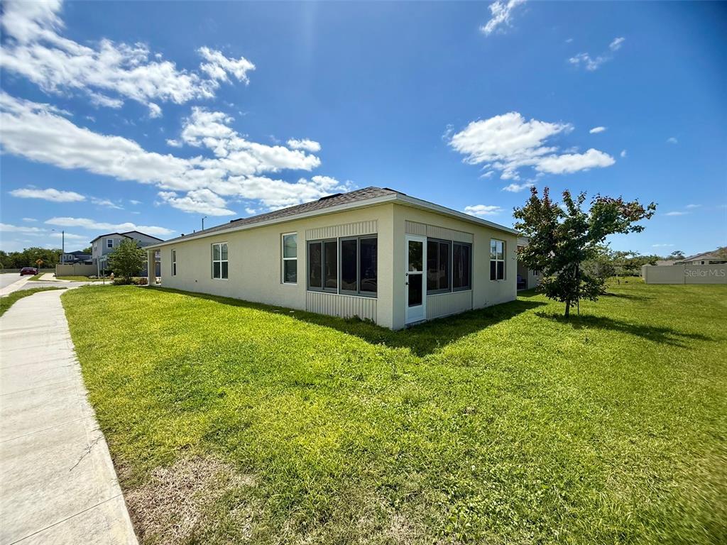 A side view of a tan house with a screened-in porch and a grassy yard — 2415 BRASSIE COURT, WINTER HAVEN, FL