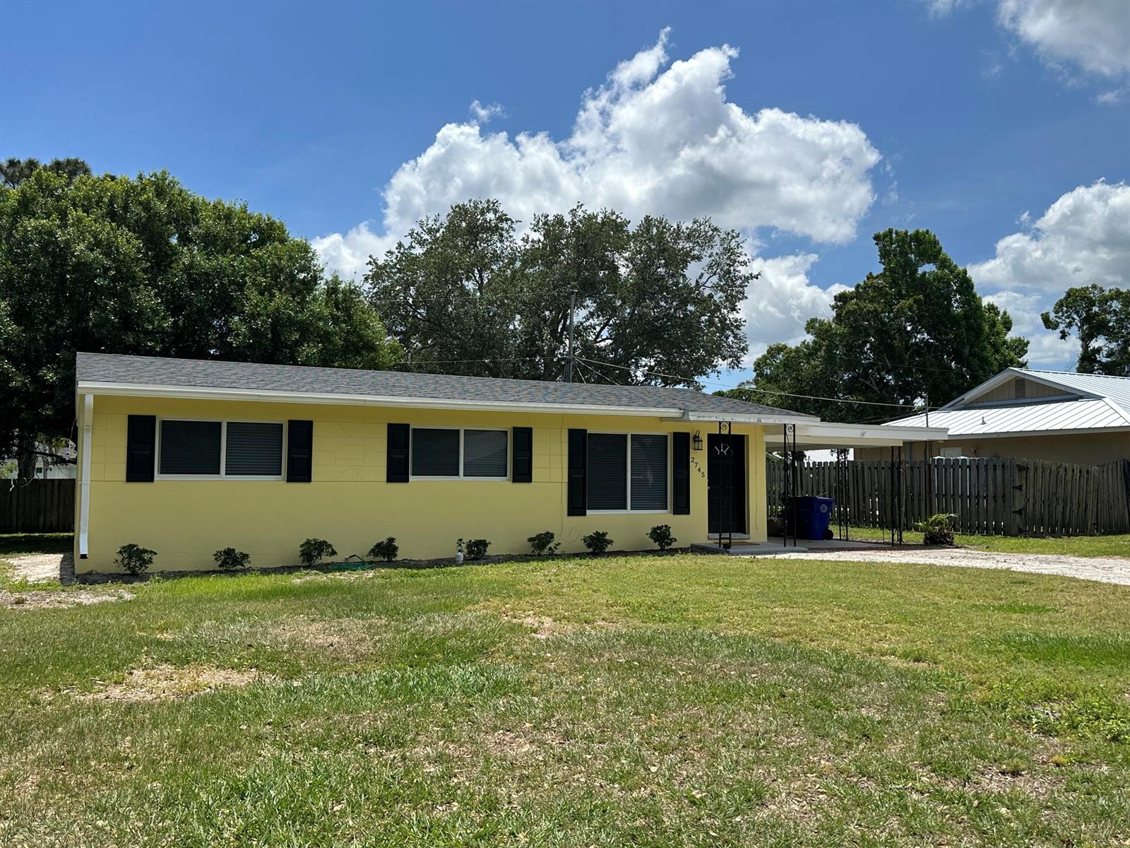 A yellow single-story house with black shutters and a carport sits on a grassy lot — 2745 Atlantic Boulevard, Vero Beach FL 32960, VERO BEACH, FL