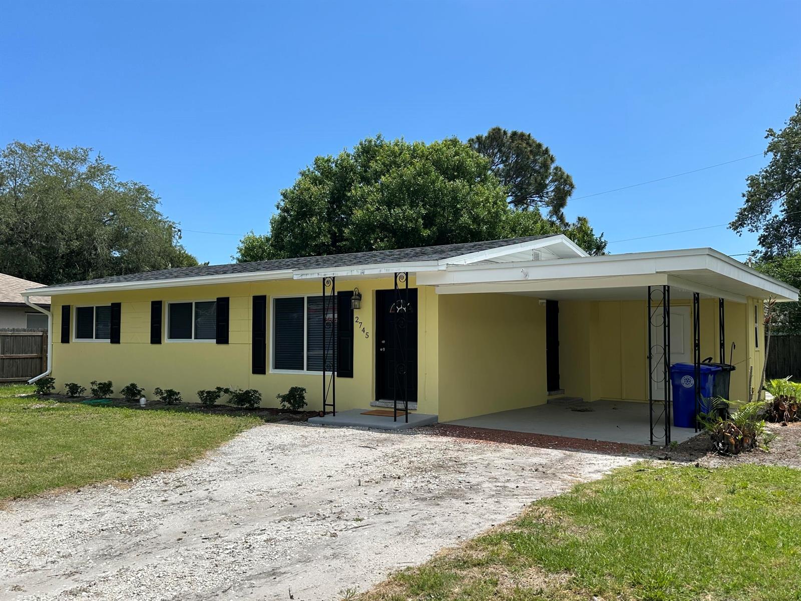 A yellow single-story house features a black front door, black shutters, and an attached carport — 2745 Atlantic Boulevard, Vero Beach FL 32960, VERO BEACH, FL