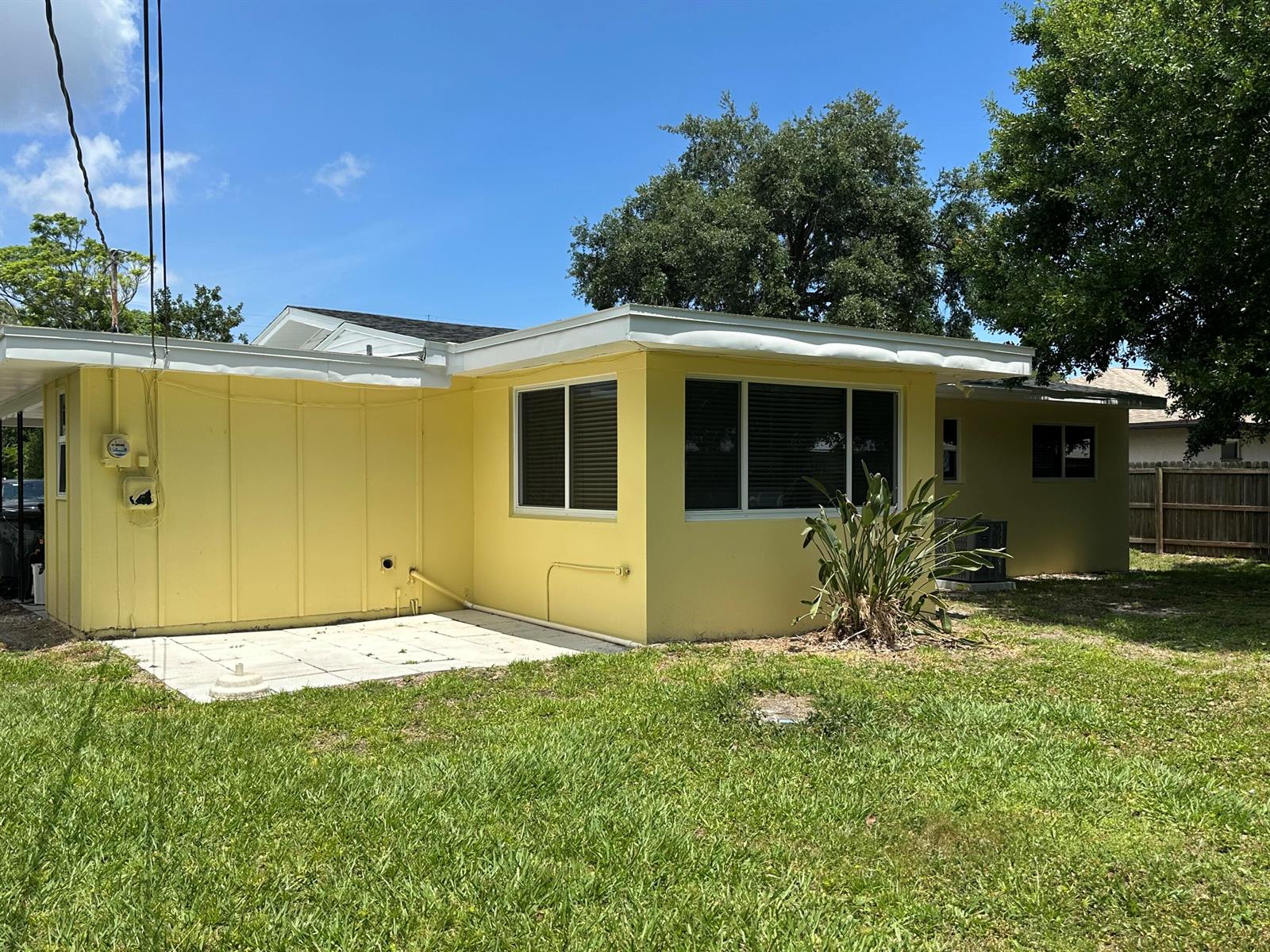A yellow house exterior features a flat roof, white trim, and a small concrete patio — 2745 Atlantic Boulevard, Vero Beach FL 32960, VERO BEACH, FL