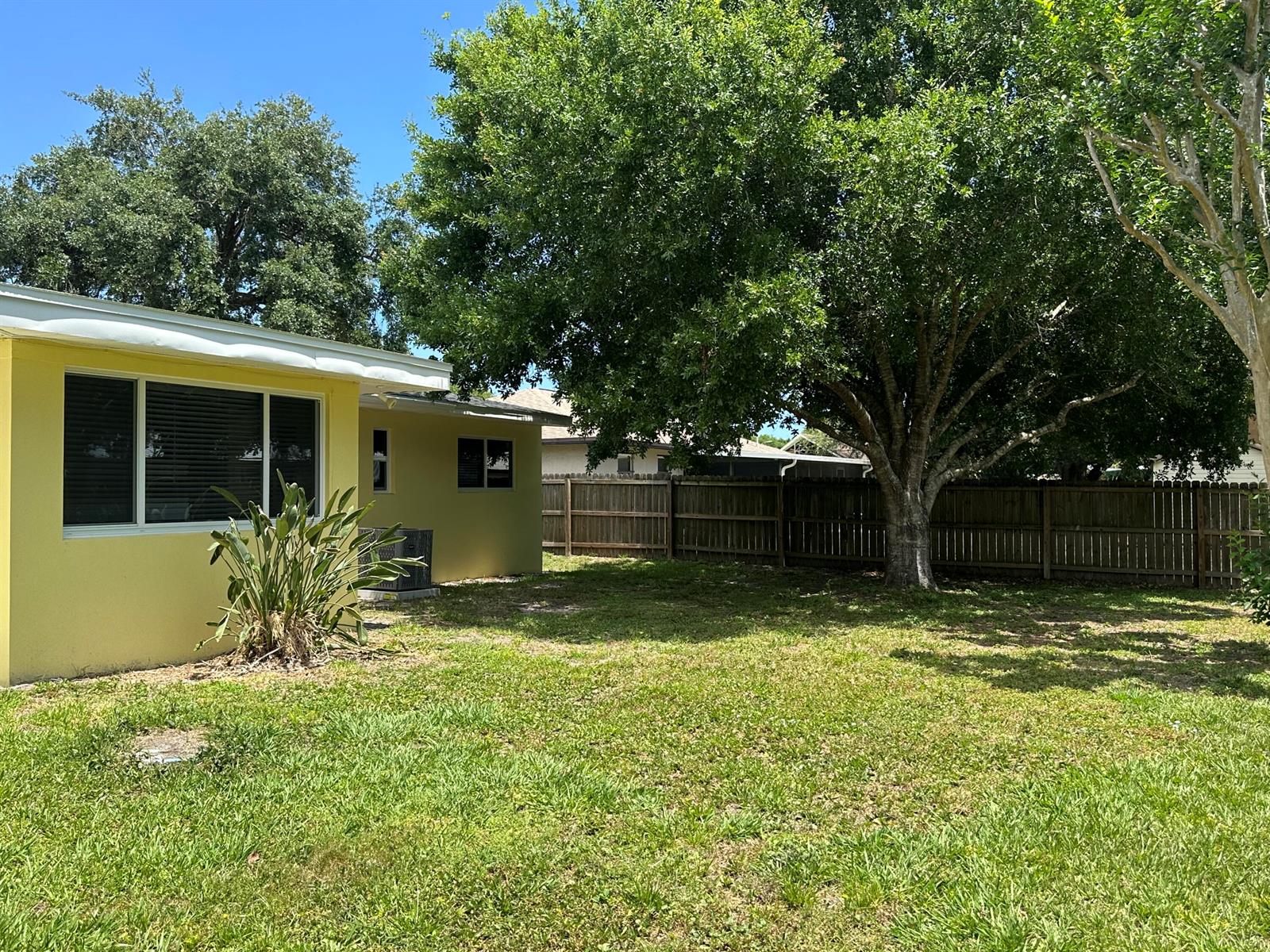A yellow house exterior features a grassy backyard with a large tree and wooden fence — 2745 Atlantic Boulevard, Vero Beach FL 32960, VERO BEACH, FL