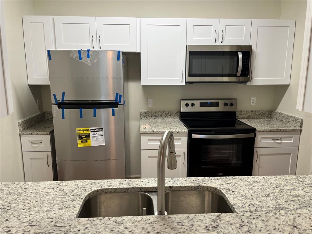A kitchen features white cabinets, stainless steel appliances, and speckled granite countertops — 3190 DANTE DRIVE UNIT 308, ORLANDO, FL