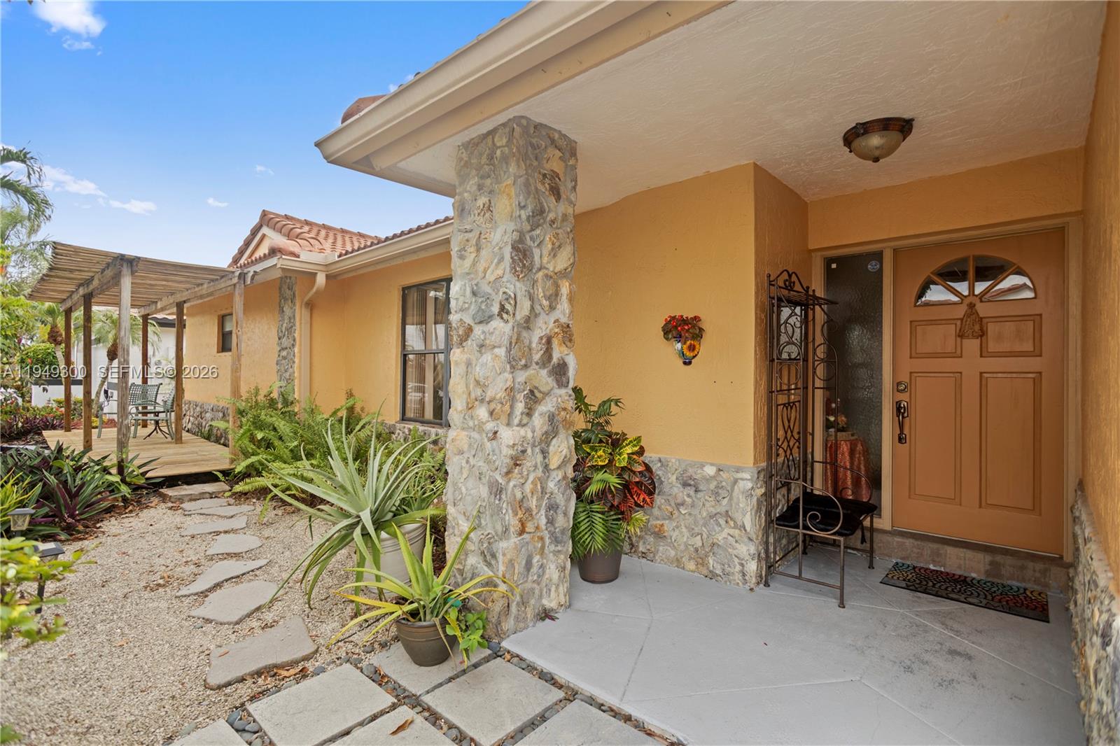 A stone-accented house exterior features a covered entryway, a wooden pergola, and a gravel path — 15824 Cotswold Ct, Davie FL 33331, DAVIE, FL