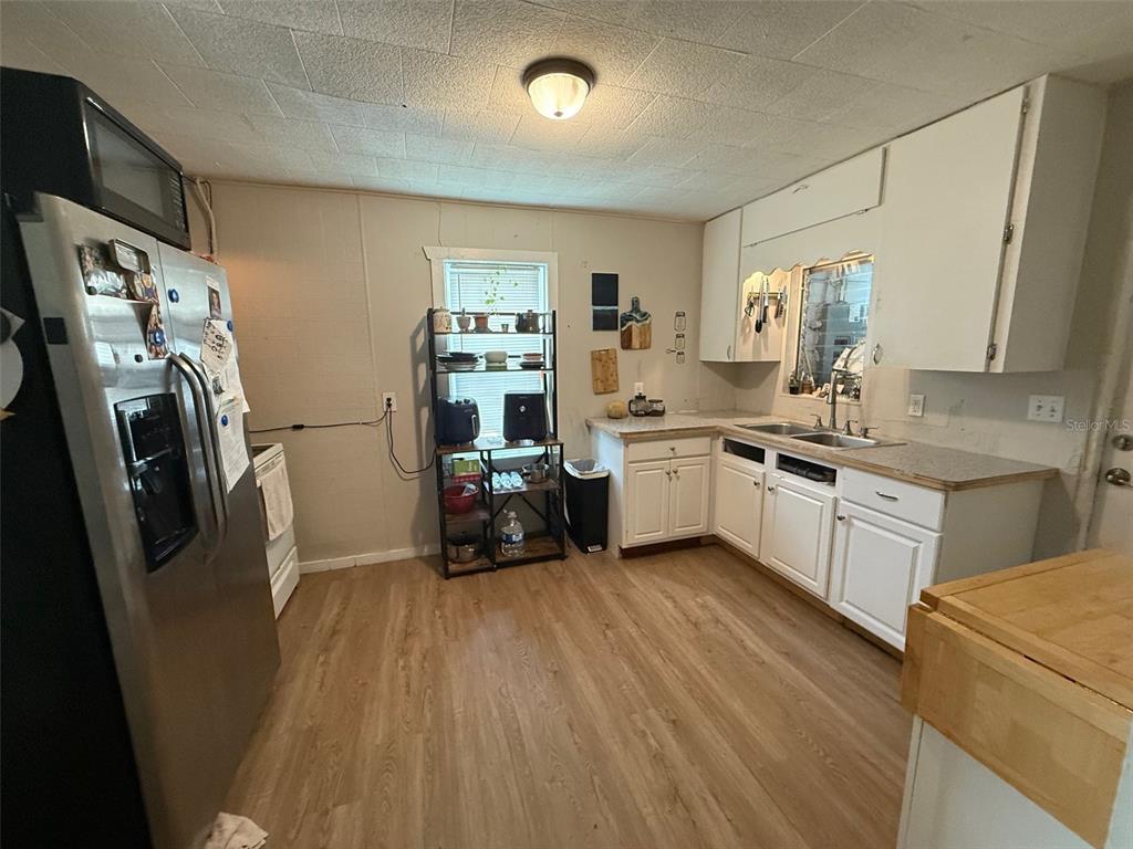A kitchen features white cabinets, a stainless steel refrigerator, and light wood-look flooring — 1222 GOLCONDA ROAD, LAKELAND, FL