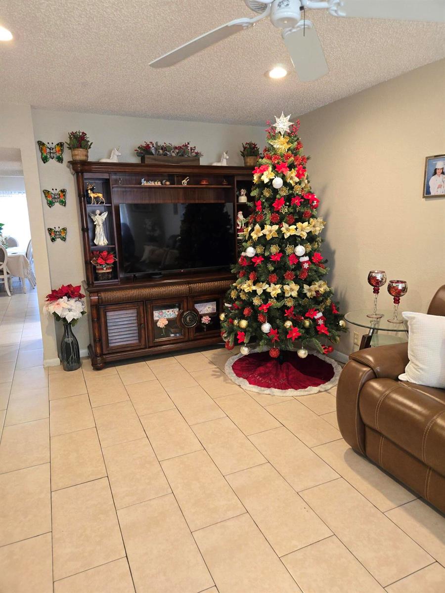 A living room features a large entertainment center, a decorated Christmas tree, and tile flooring — 2396 Daphne Drive, West Palm Beach FL 33415, WEST PALM BEACH, FL