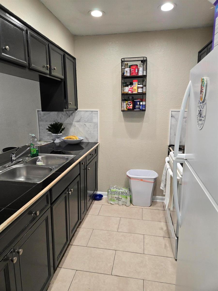 A galley kitchen features black cabinets, dark countertops, a double sink, and a wall-mounted spice rack — 2396 Daphne Drive, West Palm Beach FL 33415, WEST PALM BEACH, FL