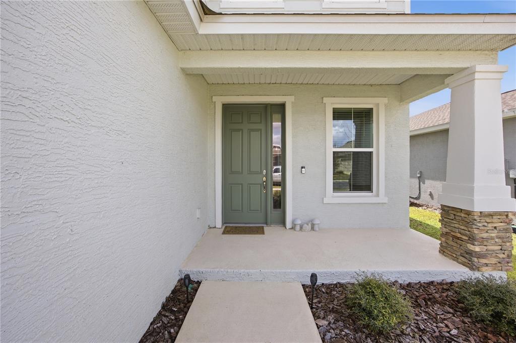 A covered concrete porch leads to a sage green front door with a side window — 7238 SW 60TH LANE, OCALA, FL