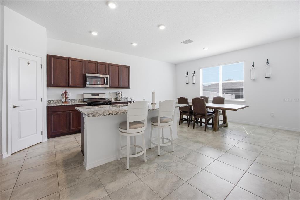 A kitchen with dark wood cabinets, granite countertops, an island with stools, and a dining area — 7238 SW 60TH LANE, OCALA, FL