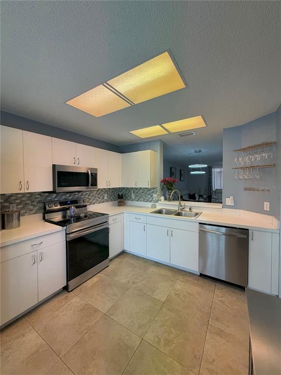 A kitchen features white cabinets, stainless steel appliances, a tiled backsplash, and light-colored floor tiles — 2122 CLOVER HILL ROAD, PALM HARBOR, FL