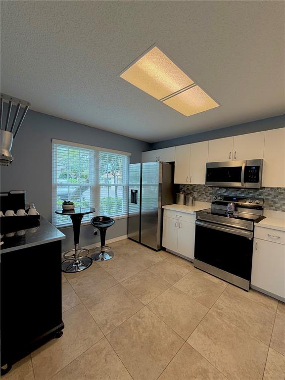 A kitchen features white cabinets, stainless steel appliances, a small bistro table, and tile flooring — 2122 CLOVER HILL ROAD, PALM HARBOR, FL