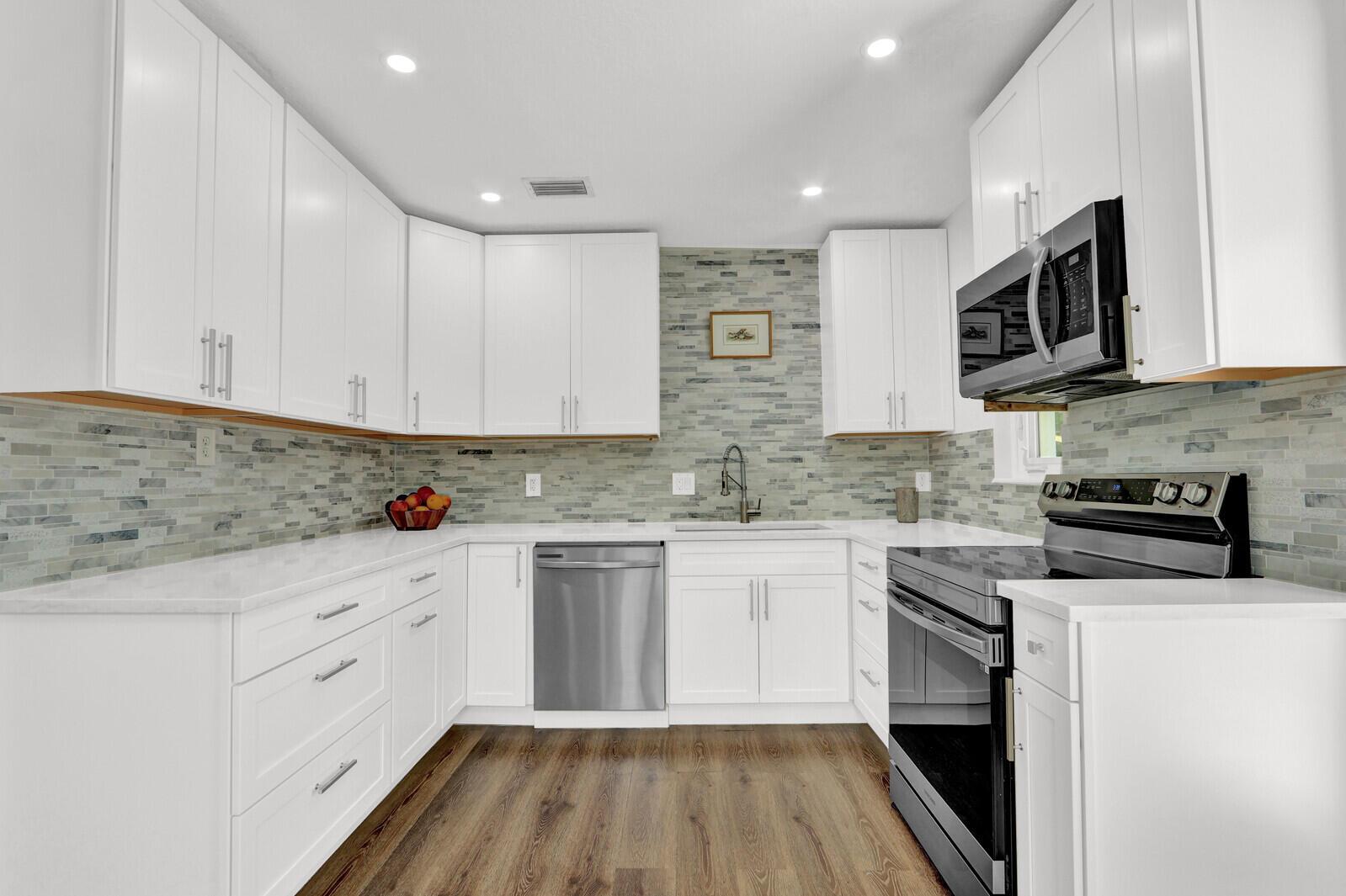 A modern kitchen features white cabinets, stainless steel appliances, and a gray tiled backsplash — 222 Bayberry Drive, Lake Park FL 33403, LAKE PARK, FL