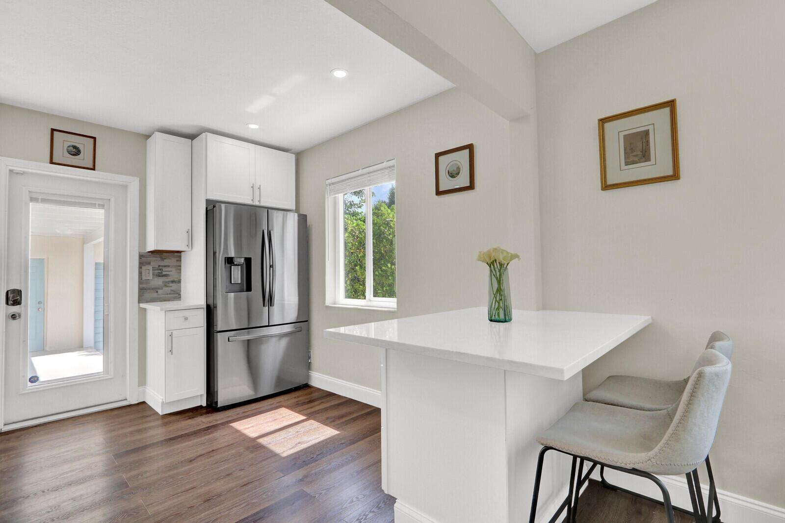 A kitchen features white cabinetry, a stainless steel refrigerator, and a small white breakfast bar — 222 Bayberry Drive, Lake Park FL 33403, LAKE PARK, FL