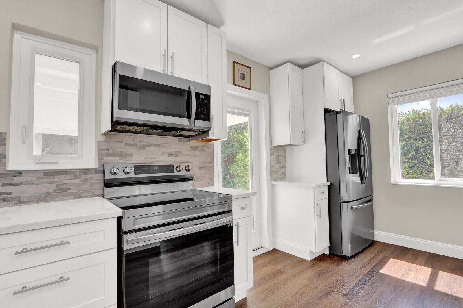 A kitchen features white cabinets, stainless steel appliances, a tiled backsplash, and wood-look flooring — 222 Bayberry Drive, Lake Park FL 33403, LAKE PARK, FL