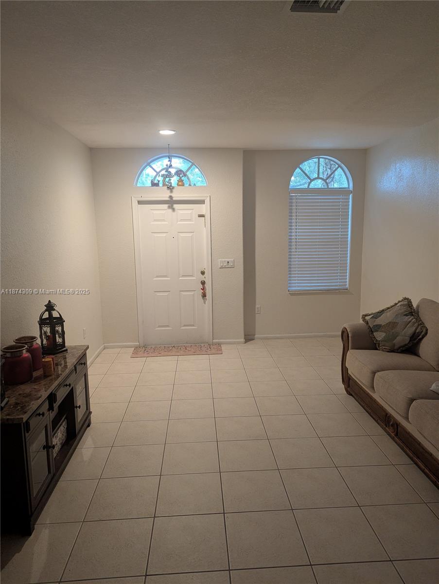 A living room features light tile flooring, a front door with a transom, and a sofa — 8496 SW 29th St # 104, Miramar FL 33025, MIRAMAR, FL
