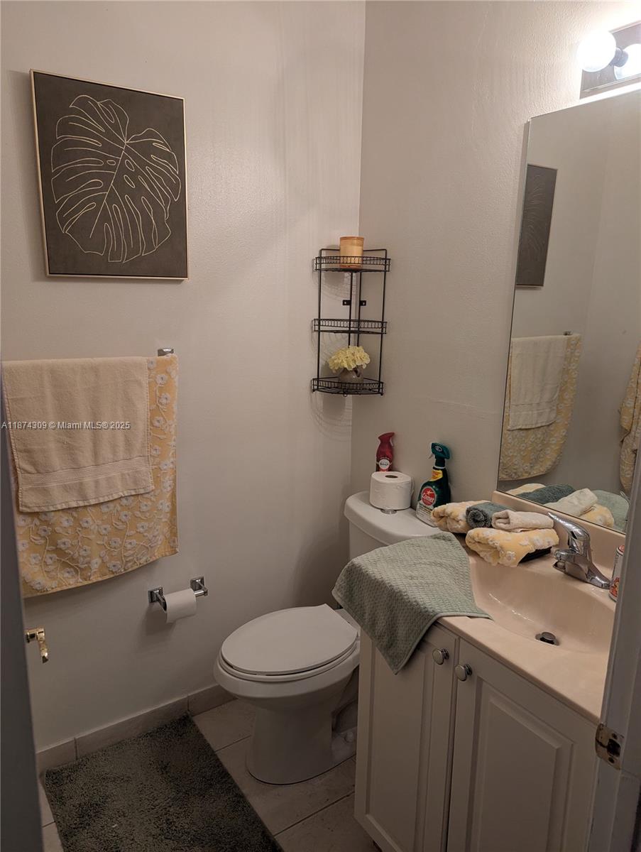 This bathroom features a white vanity, a toilet, a wall-mounted shelf, and floral-patterned towels — 8496 SW 29th St # 104, Miramar FL 33025, MIRAMAR, FL