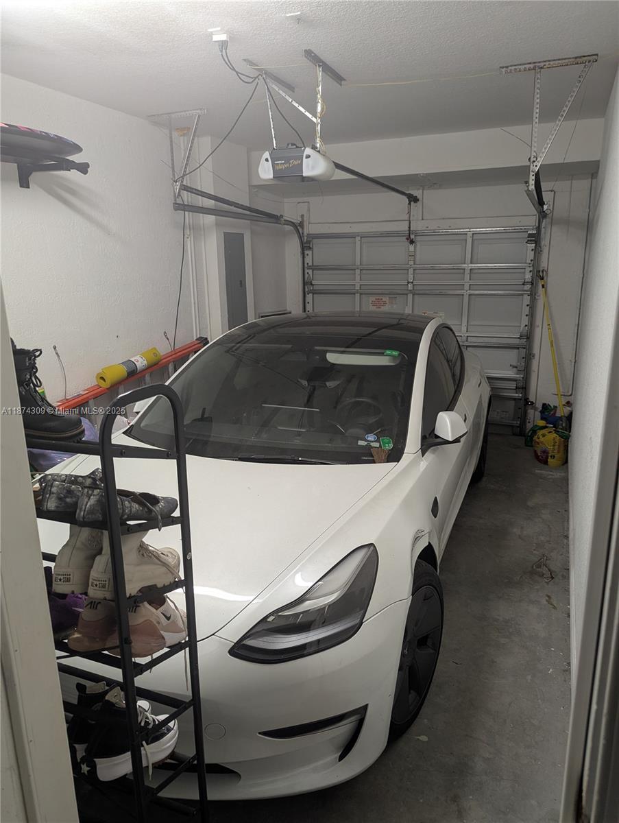 A white Tesla is parked inside a residential garage with a shoe rack in the foreground — 8496 SW 29th St # 104, Miramar FL 33025, MIRAMAR, FL