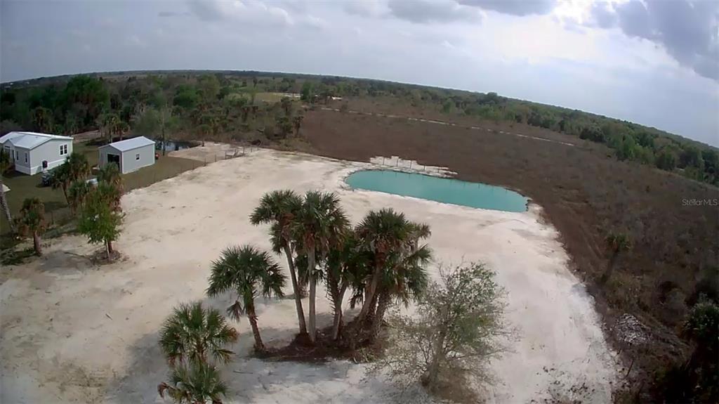 An aerial view shows a sandy lot with palm trees, a pond, and two buildings — 19374 NW 302ND STREET, OKEECHOBEE, FL
