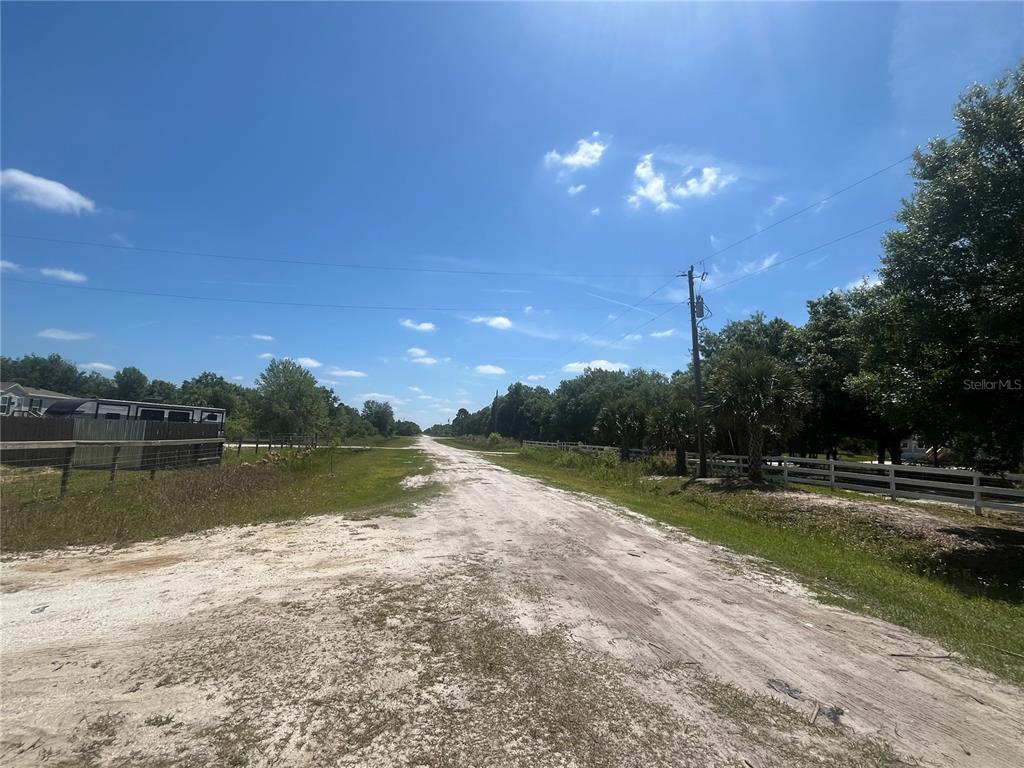 A dirt road stretches into the distance between a fenced property and wooded areas — 19374 NW 302ND STREET, OKEECHOBEE, FL