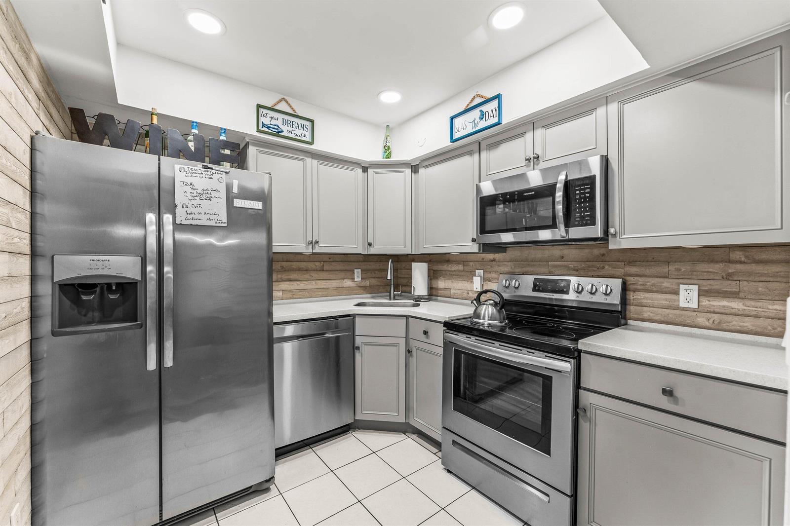 A kitchen features gray cabinets, stainless steel appliances, a wood-plank backsplash, and white tile flooring — 950 S Kanner Highway # 10, Stuart FL 34994, STUART, FL